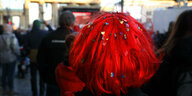 Eine Person mit roter Perücke und Konfetti im Haar vor dem Brandenburger Tor