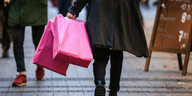 Eine Person geht mit rosa Einkaufstüten durch eine Fußgängerzone, man sieht nur den Unterkörper
