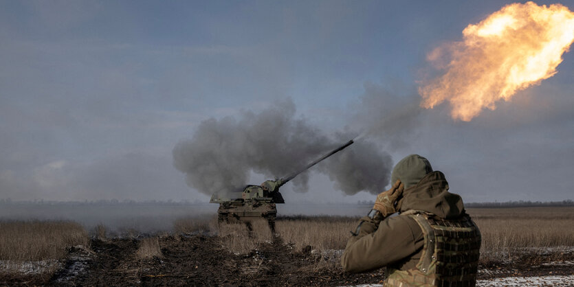 Panzerhaubitze schießt, davor ein Soldat.