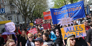 Teilnehmer einer Demonstration zum 1. Mai unter dem Motto „Klassensturz statt Kassensturz“ ziehen mit einem Banner mit der Aufschrift „Reichensteuer Jetzt!“ durch die Straßen im Stadtteil Harvestehude