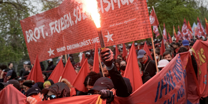 Ein Mann in einem Demozug hält ein brennendes Bengalo in der Hand