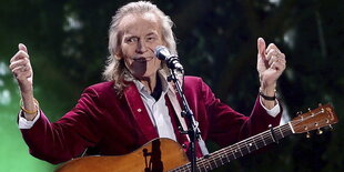 Gordon Lightfoot steht auf einer Büne in Ottawa, eine Gitarre um den Hals, beide Daumen nach oben gestreckt-