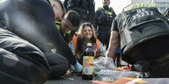 Eine Klimaaktivistin sitzt auf einer Straße, umgeben von Polizisten