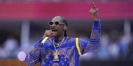 Snoop Dogg mit Mikrofon in der einen Hand, mit der anderen streckt er den Zeigefinger nach oben