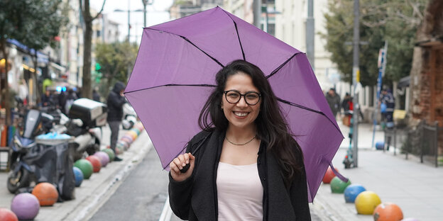 Sera Kadıgilhält einen lila farbenen Regenschirm und lächelt in die Kamera