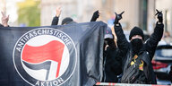 Eine Gruppe vermummter Demonstranten zeigt den Mittelfinger, teilweise verdeckt von einer Antifa-Flagge