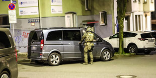 Ein Polizist steht während einer Razzia an einem Van.