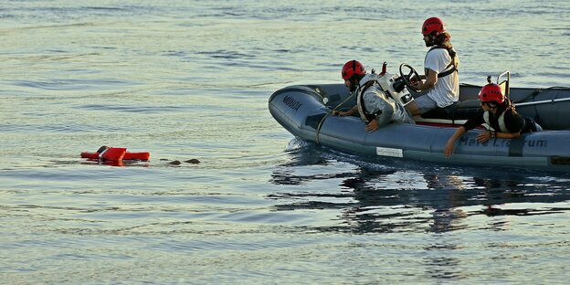 Ein Mensch in oranger SChwimmweste im Wasser und 3 Menschen mit Helmen in einem Schlauchboot mit Motor der Organisation Mare Liberum