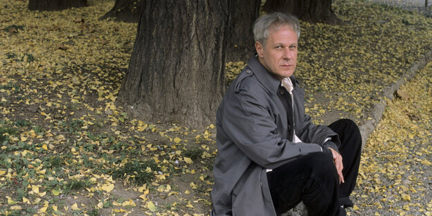 Der Autor Dennis Cooper sitzt im Wald und blickt in die Kamera