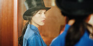 Das Spiegelbild einer dunkelhaarigen Frau mit Zopf, Zylinder und blauer Bluse