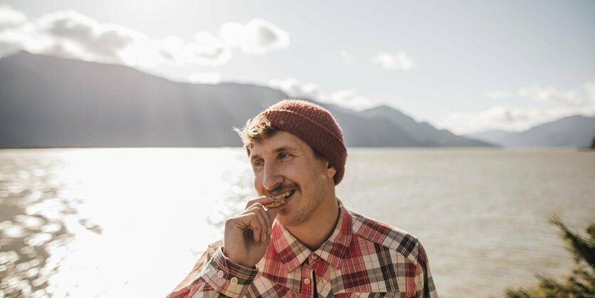 Eine Person steht vor einem Bergsee und isst einen Keks