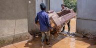 Menschen tragen ihre Habseligkeiten über eine mit braunem Wasser geschwemmte Straße