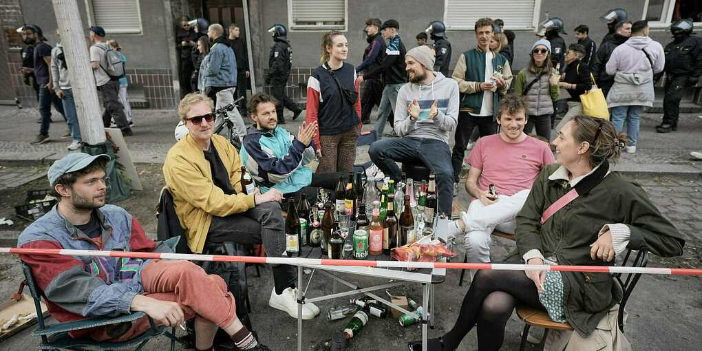 Junge Menschen sitzen an der Wegstrecke eines Demonstrationszuges an Tischen