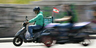 Ein Lieferbote fährt mit Helm auf einem Moped, auf dem eine kleine syrische Flagge im Fahrtwind weht