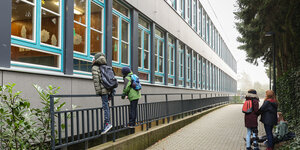 Kinder mit Schulranzen gucken von Draußen in ein Schulgebäude
