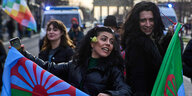 Zwei Demonstrant*innen halten jeweils eine Romaflagge. Im Hintergrund ist das Brandenburger Tor zu sehen