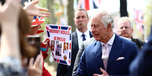 König Charles schüttelt Hände und jemand zeigt ihm ein selbst gebasteltes Plakat: Mummy would be proud