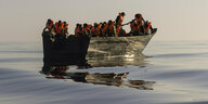Migranten sitzen mit Rettungswesten in einem Boot