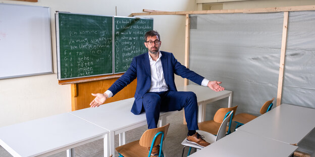 Jens Marco Scherf sitzt in einem leeren Klassenzimmer vor einer Schultafel