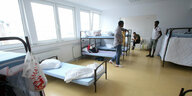 Drei Geflüchtete stehen in einem Vielbettzimmer mit Hochbetten in einer Unterkunft in Nordrhein-Westfalen
