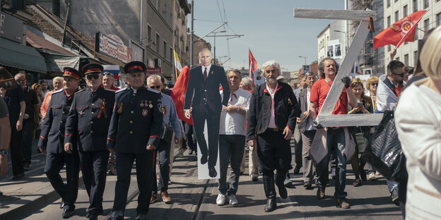 Demonstranten in einer Reihe mit militärischer Uniform, eine Putin-Pappfigur und ein großes silbernes Z wird getragen