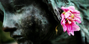 Eine Blume steckt im Ohr der Statue "Die Kugelspielerin" in einem Park in Düsseldorf.