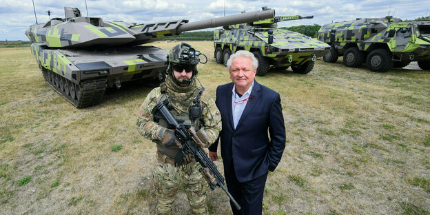 Armin Papperger posiert mit einem Soldaten vor Panzern