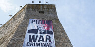 An der Festungsmauer in Narwa hängt ein Plakat mit dem Porträt von Putin da mit roter Farbe beworfen wurde: "War Criminal"