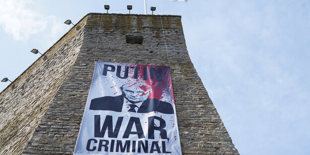 An der Festungsmauer in Narwa hängt ein Plakat mit dem Porträt von Putin da mit roter Farbe beworfen wurde: "War Criminal"