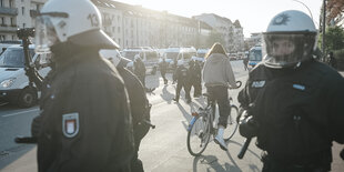 Zwei Polizisten mit Helm blicken in die Kamera. Im Hintergrund liegt ein Verletzter