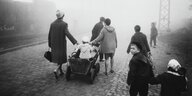 Ein Mann und eine Frau neben vielen Kindern auf einem Bahnsteig, ein Bollerwagen wird gezogen, neblige Stimmung, ein Junge dreht sich um, neben ihm an der Hand ein kleineres Kind