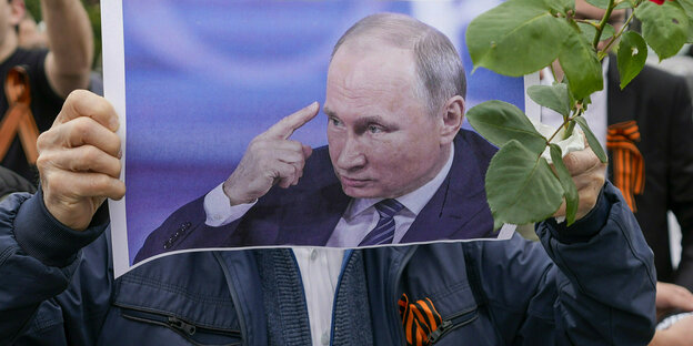 Eine Person hält sich das Portrait Wladimir Putins vor das Gesicht