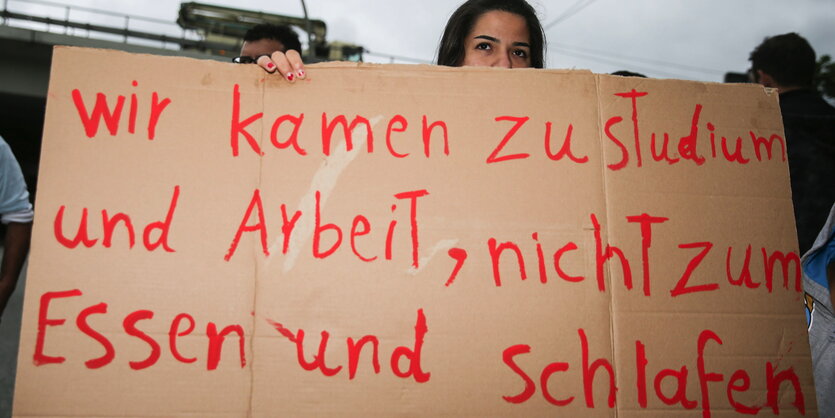 Eine Flüchtlingsfrau in einer Hamburger Flüchtlingsunterkunft hält ein Schild hoch „Wir kamen zu Studium und Arbeit, nicht zum Essen und Schlafen“