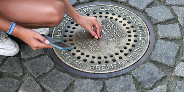 Eine frau wirft eine Münze in den bekannten Strassengulli "Bremer Loch".