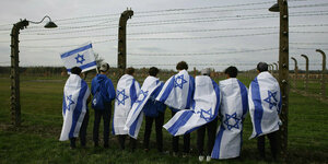 Personen stehen in israelischen Fahnen gewandt an einem Zaun