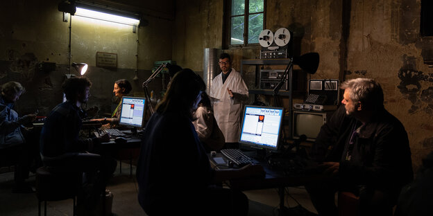 Szene im dunklen Keller-Labor vor Bildschirmen und Mann mit weißen Kittel