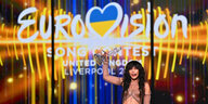 Eine Frau hält einen Pokal in der Hand, im Hintergrund steht Eurovision mit V als Herzchen