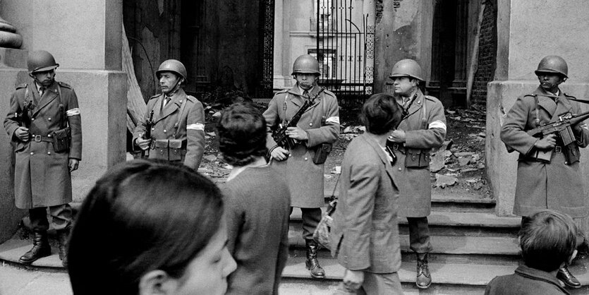 Ein schwarz-weiß Foto von Soldaten, die in einer Reihe stehen und Menschen, die an ihnen vorbeigehen