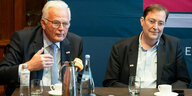 2 Männer bei einer Pressekonferenz mit Kaffeetassen auf dem Tisch