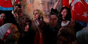 Menschen mit ürkischen Fahnen vor einem Plakat mit dem Porotrait Erdogans