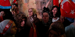 Menschen mit ürkischen Fahnen vor einem Plakat mit dem Porotrait Erdogans