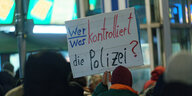 Ein Teilnehmer einer Kundgebung des Bündnis Köln gegen Rechts gegen Polizeigewalt trägt ein Plakat mit der Aufschrift "Wer/was kontrolliert die Polizei"
