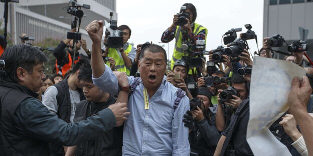 Jimmy Lai mit erhobener Faust , hinter ihm eine Gruppe Fotografen