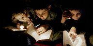 Drei Kinder lesen im Schein ihrer Taschenlampen ein Buch