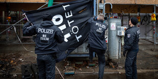 Polizisten entfernen ein Banner von einem Gebäude, auf dem Banner steht "110 tötet"