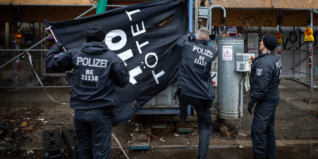 Polizisten entfernen ein Banner von einem Gebäude, auf dem Banner steht "110 tötet"