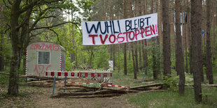 Drei Polizisten stehen vor dem Protestcamp in der Wuhlheide und schauen auf ein Baumhaus