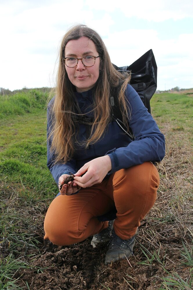 Die Moormanagerin Annie Wojatschke kniet auf dem Boden und hält eine Bodenprobe in der Hand