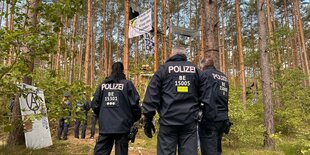 Polizisten stehen im Wald, über ihnen Transparente, Aufschrift: Friede den Nestern, Krieg den Palästen