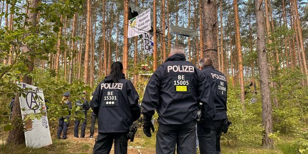 Polizisten stehen im Wald, über ihnen Transparente, Aufschrift: Friede den Nestern, Krieg den Palästen